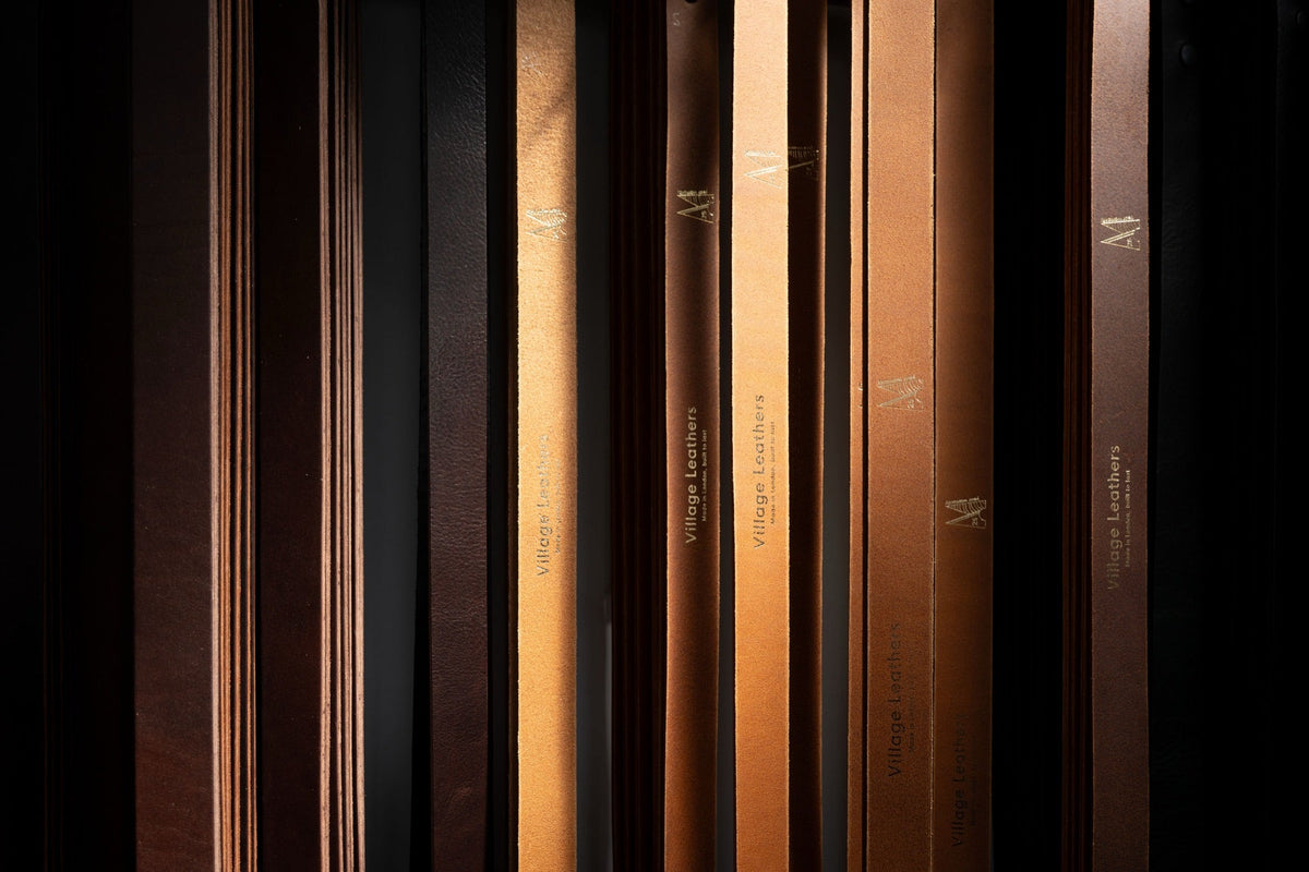 Leather belt straps hanging in the workshop, gold-embossed Village Leathers, made in London